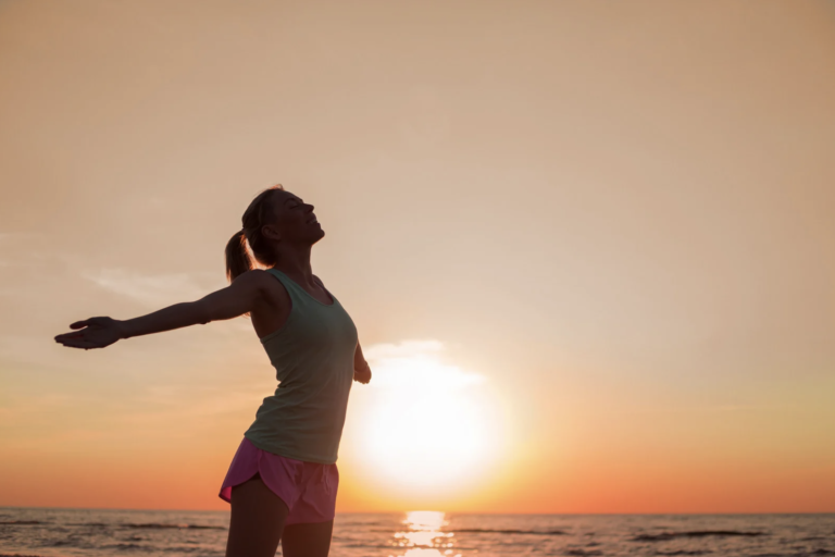 Woman enjoying a peaceful sunrise by the ocean with arms outstretched